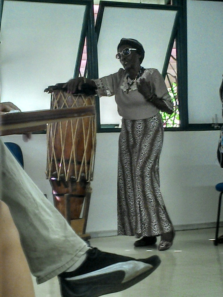 Dona Tiana fala à comunidade universitária sobre sua história, apoiada no instrumento musical que trouxe de sua comunidade.